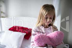 Girl holding heart shape pillow on bed