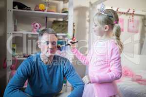 Cute daughter in fairy costume putting makeup on her fathers face