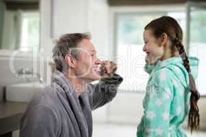 Smiling father and daughter brushing teeth in bathroom