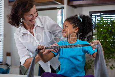 Physiotherapist assisting girl patient in performing stretching exercise from resistance band