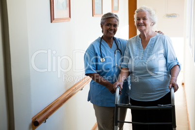 Portrait of nurse assisting senior patient in walking with walker