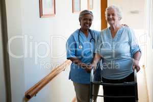 Portrait of nurse assisting senior patient in walking with walker