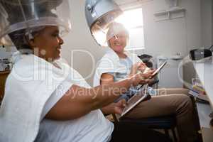 Friends using digital tablet while sitting under hair steamer