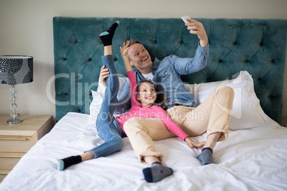 Smiling father and daughter taking selfie with mobile phone on bed