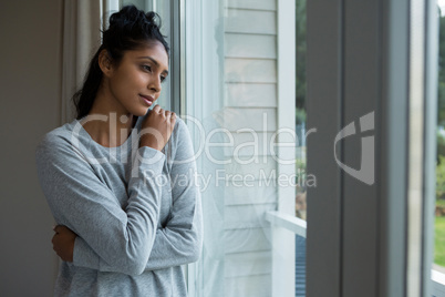 Thoughtful woman with hand on shoulder by window