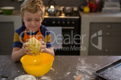 Boy kneading dough over yellow bowl