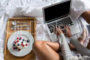 Low section of woman using laptop by breakfast on bed