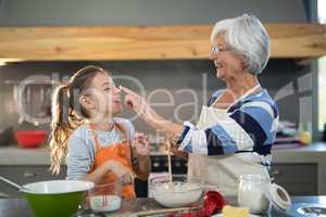 Grandmother putting flour on granddaughters nose