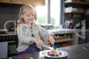Little girl cutting a fruit pancake with a fork and knife