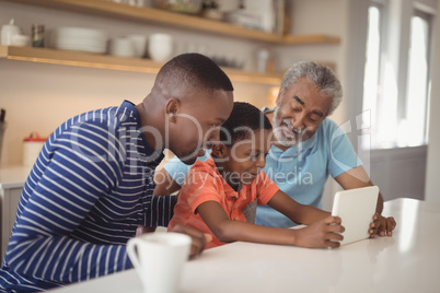 Happy multi-generation family using digital tablet in kitchen