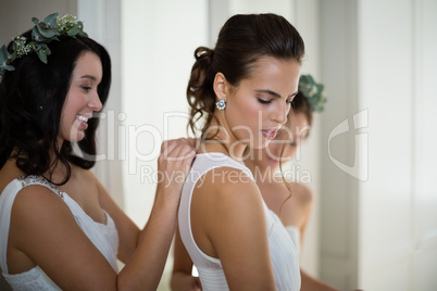Bridesmaid assisting bride to dress
