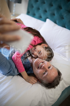 Smiling father and daughter taking selfie with mobile phone on bed