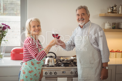 Smiling senior couple toasting glasses of wine in kitchen