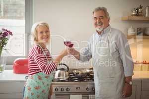 Smiling senior couple toasting glasses of wine in kitchen