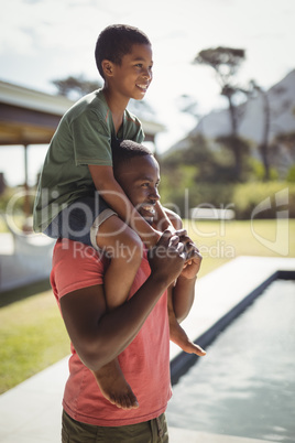 Father carrying son on shoulders near poolside