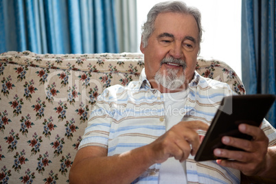 Smiling senior man using digital tablet while sitting on sofa