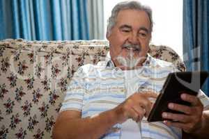 Smiling senior man using digital tablet while sitting on sofa