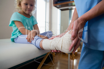 Physiotherapist putting bandage on injured feet of girl patient