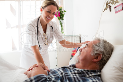 Doctor examining senior man lying on bed in nursing home