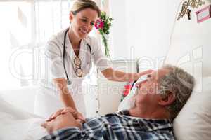 Doctor examining senior man lying on bed in nursing home
