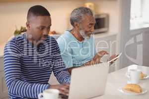 Father and son using laptop and digital tablet in kitchen