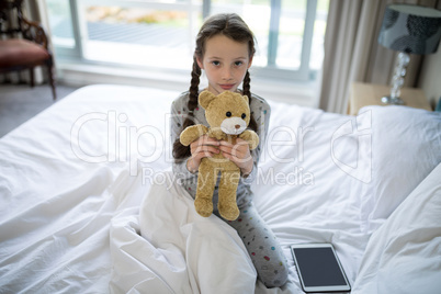 Girl holding teddy bear on bed in bedroom