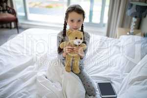Girl holding teddy bear on bed in bedroom