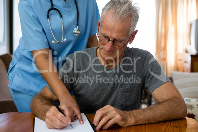 Female doctor assisting senior man in writing at nursing home