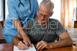 Female doctor assisting senior man in writing at nursing home
