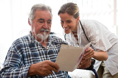 Female doctor showing greeting card to patient sitting on wheelchair