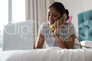Woman using laptop while talking on phone on bed