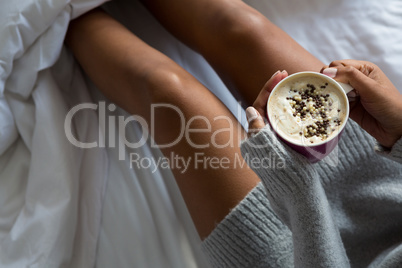 Mid section of woman having coffee on bed