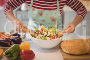 Senior woman mixing vegetables salad in kitchen