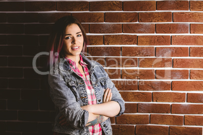 Smiling woman standing with arms crossed against brick wall