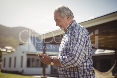 Senior man checking his mobile phone outside his house.