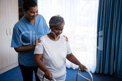 Nurse hepling senior woman in walking with walker