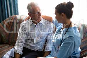 Doctor consoling senior man while sitting on sofa