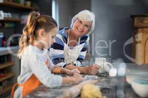Granddaughter flattening dough with grandmother