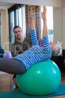 Physiotherapist assisting senior woman in performing exercise on fitness ball