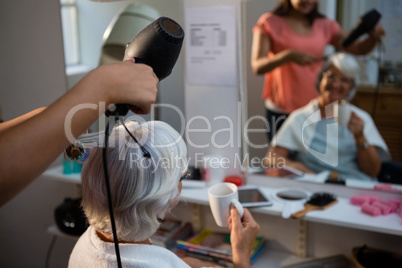 Beautician drying senior woman hair reflecting on mirror