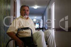 Portrait of senior man sitting on wheelchair in corridor
