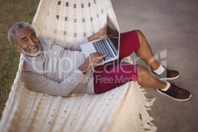 Smiling senior man using laptop while relaxing on hammock