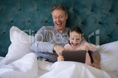 Smiling father and daughter using digital tablet on bed