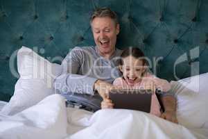 Smiling father and daughter using digital tablet on bed