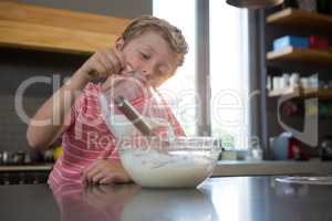 Boy pouring milk in batter at kitchen