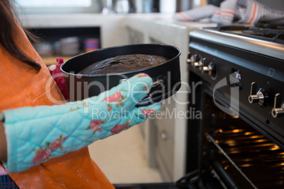 Cropped image of girl holding container with cake by oven