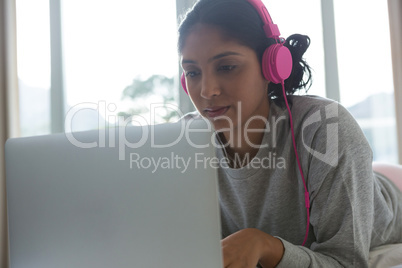 Woman listening to music while using laptop on bed