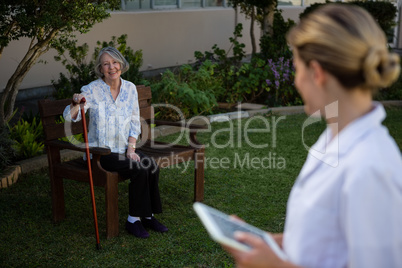 Doctor holding tablet looking at woman sitting on bench in park