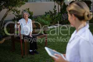 Doctor holding tablet looking at woman sitting on bench in park