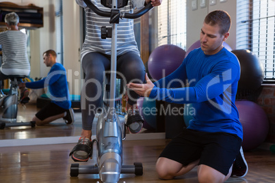 Physiotherapist assisting senior woman in performing exercise on exercise bike